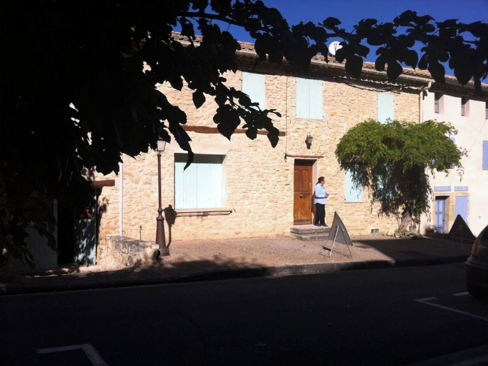 A stone building with a wooden door, a small window, and a signboard on the ground.