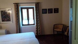 Una habitación de hotel con cama, una silla, ventana con cortinas y tres cuadros en la pared.
