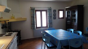 Une cuisine équipée d’une cuisinière, d’une table à manger avec des chaises, d’une fenêtre avec des rideaux et d’un meuble de rangement.