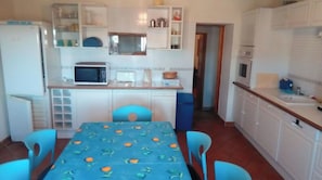 Une cuisine de taille réduite, avec des meubles blancs, un four à micro-ondes, un évier et une table recouverte d’une nappe bleue.