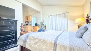 Una camera da letto con un letto, una cassettiera, una lampada e vista sulla cucina.
