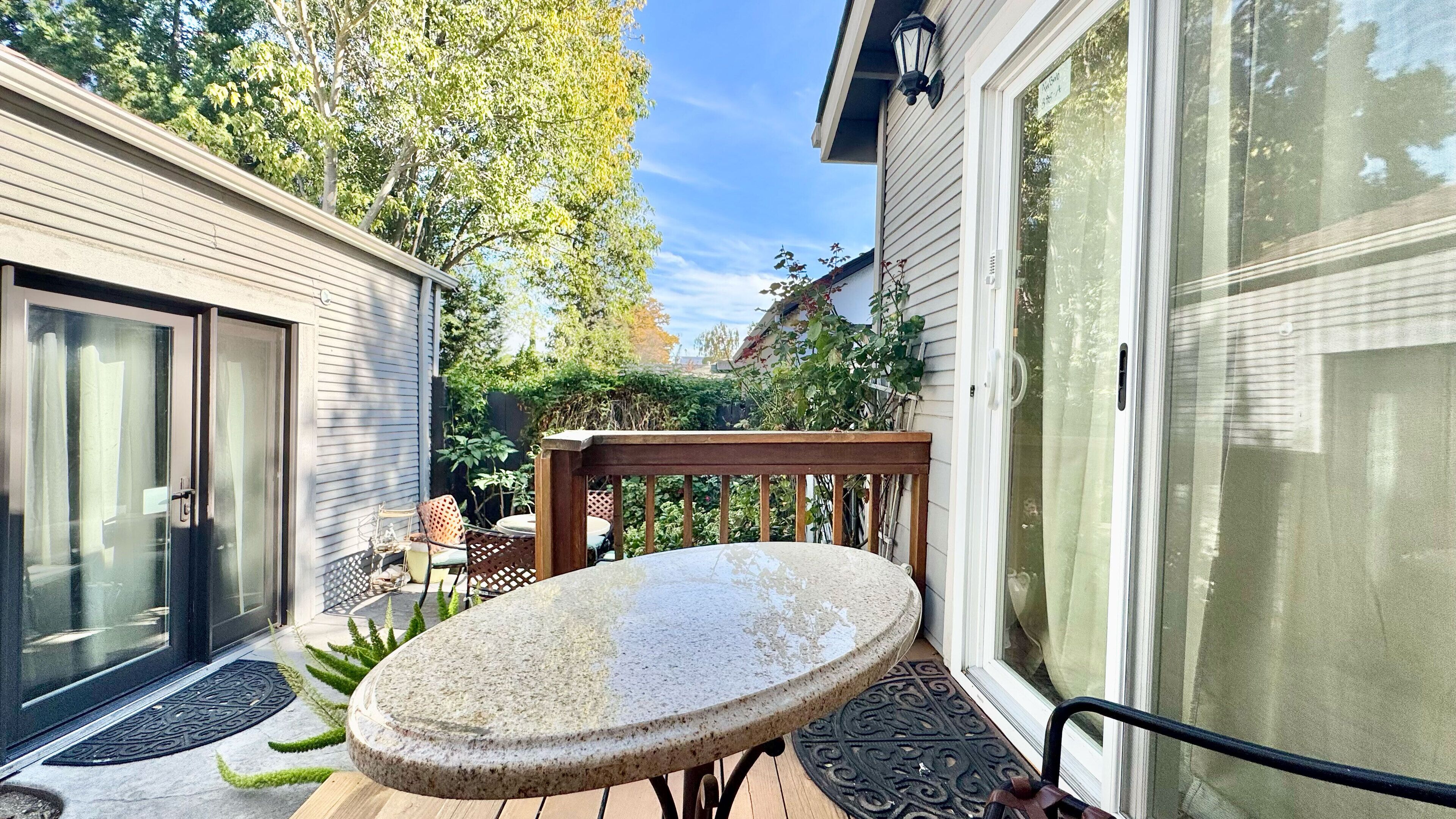 Eine Terrasse mit rundem Tisch und Stühlen, einer Holzbank und einer Schiebetür.