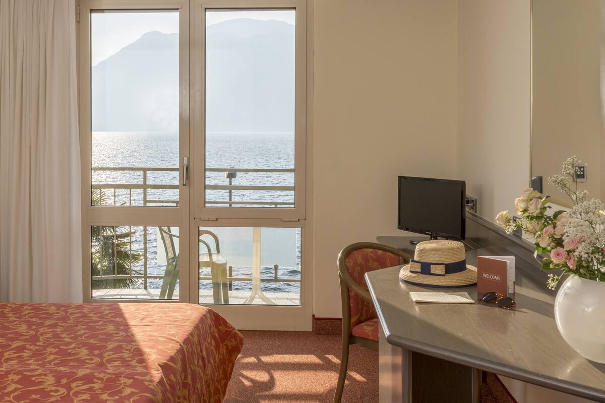 Een hotelkamer met een bed, een bureau, een televisie en uitzicht op zee.