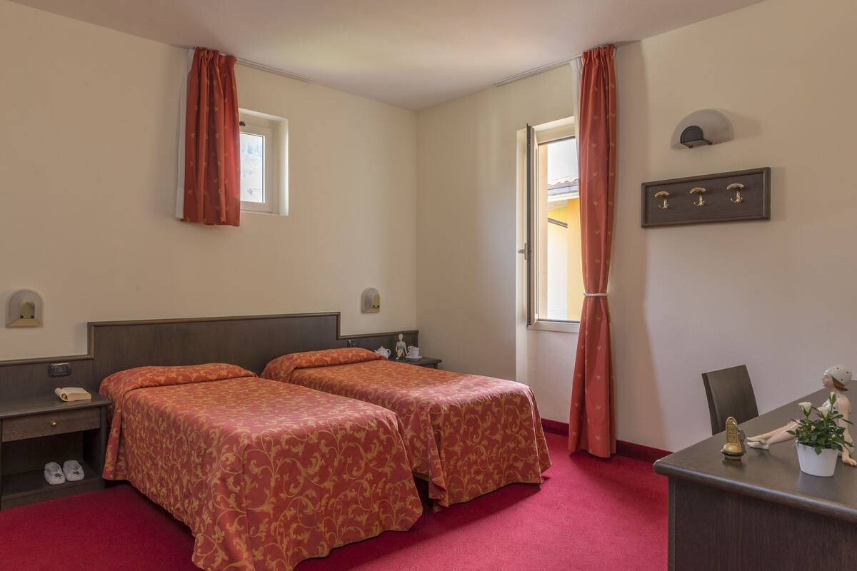 Een hotelkamer met twee bedden, een bureau, een stoel, een kleine tafel en een raam met gordijnen.