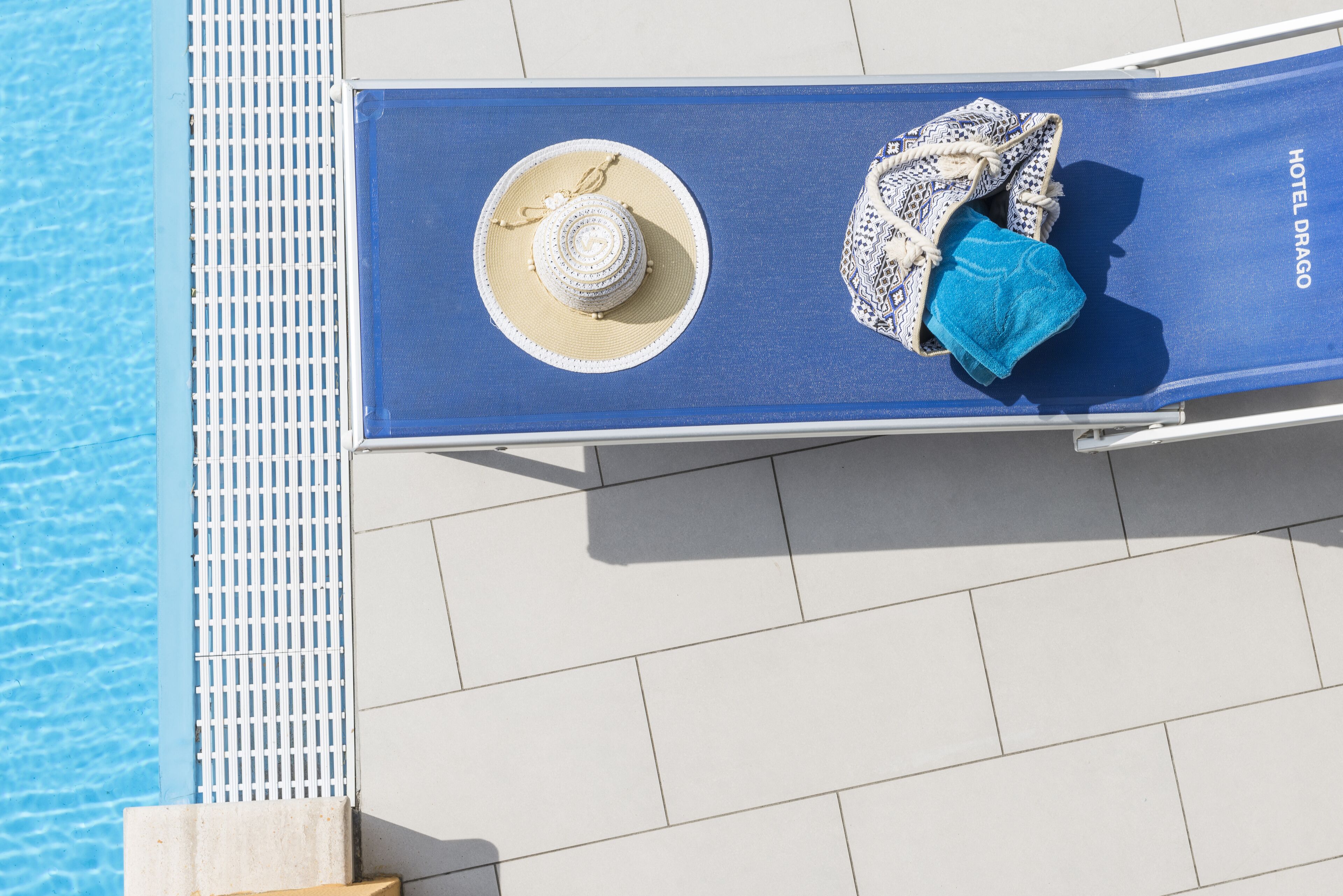 Una silla azul junto a una piscina, con un sombrero y una toalla.