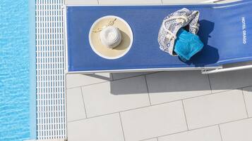 Una silla azul junto a una piscina, con un sombrero y una toalla.