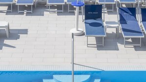 Ein Schwimmbecken mit Logo, Liegestühlen und einer Fliesenveranda.