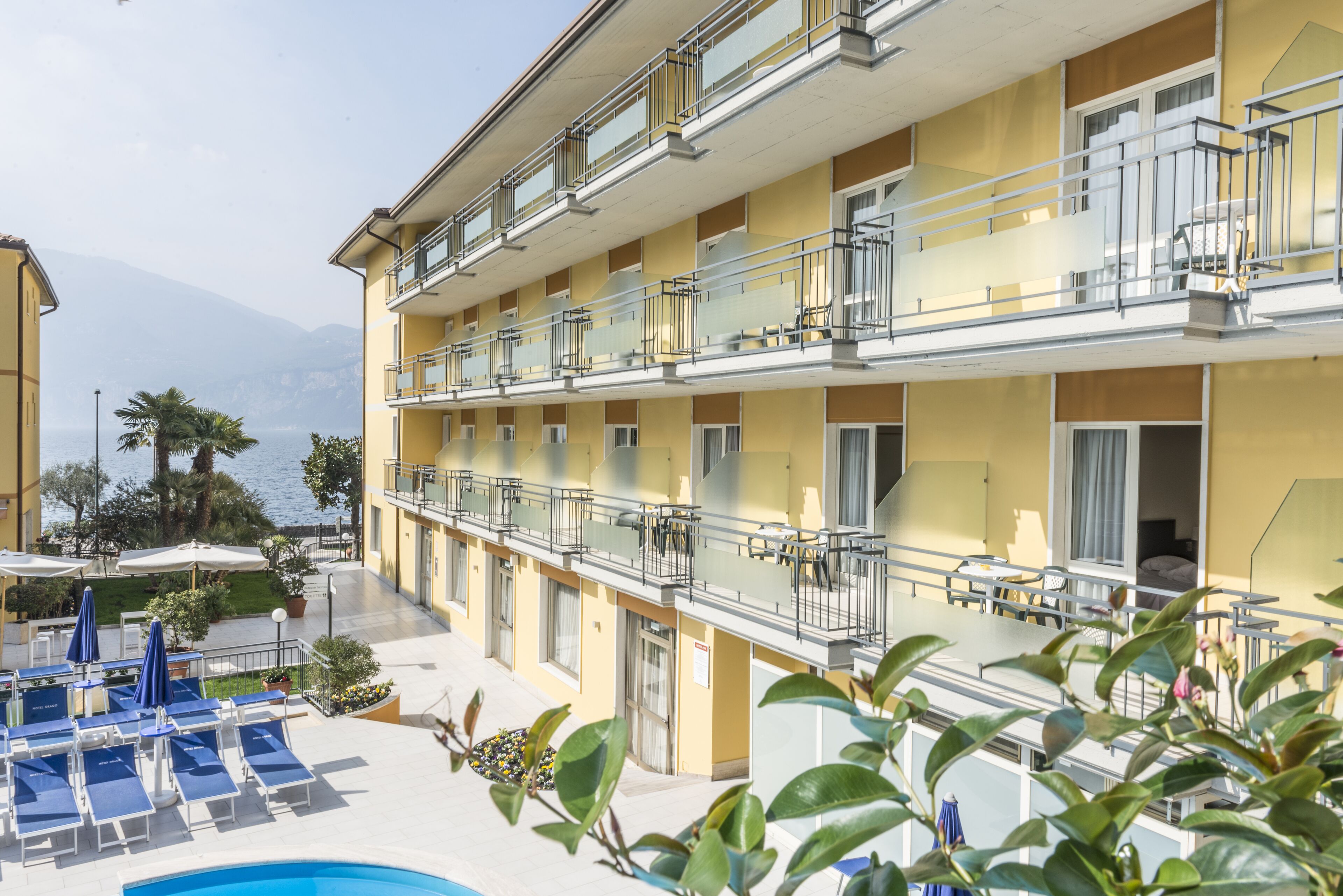 Un hotel con múltiples balcones, una zona de piscina con tumbonas y vistas al mar.