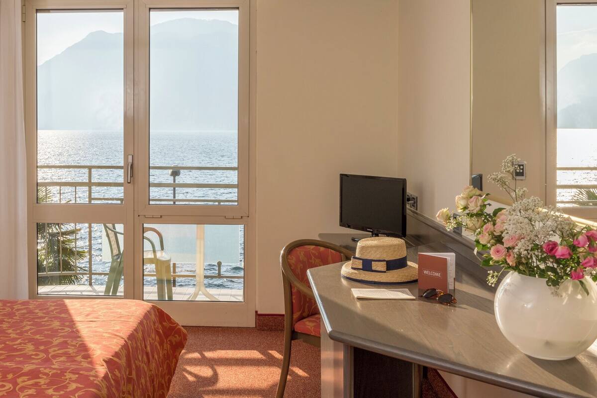 Een hotelkamer met een bed, bureau, stoel, televisie en uitzicht op zee.