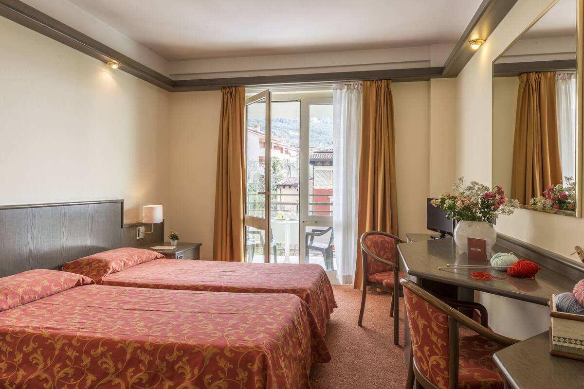 Een hotelkamer met twee bedden, een bureau, een stoel, een spiegel en uitzicht.