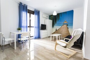 Un salon avec un plancher en bois, un téléviseur, un bureau, une chaise et une fresque représentant une scène de plage.