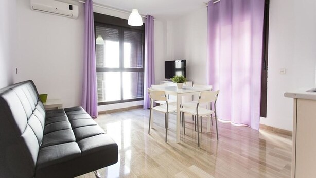 A modern living room with a sofa, a dining table with chairs, a TV, and a window with purple curtains.