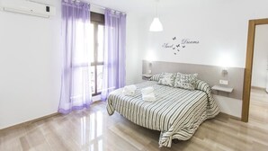 A bedroom with a bed, curtains, a wall-mounted air conditioner, a ceiling light, and a wall decal.