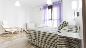 A modern bedroom with a bed, a chair, a bedside table, and a window with curtains.