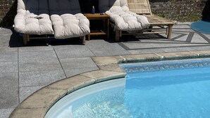 A swimming pool with a curved edge, surrounded by stone tiles and a lounge area with cushioned chairs. - Craythornes -  a holiday let by Bloom Stays that sleeps 18 guests  in 5 bedrooms (New Romney)
