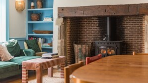 A cozy living room with a brick fireplace, a blue bookshelf, a green sofa, and a checkered table. - Craythornes -  a holiday let by Bloom Stays that sleeps 18 guests  in 5 bedrooms (New Romney)