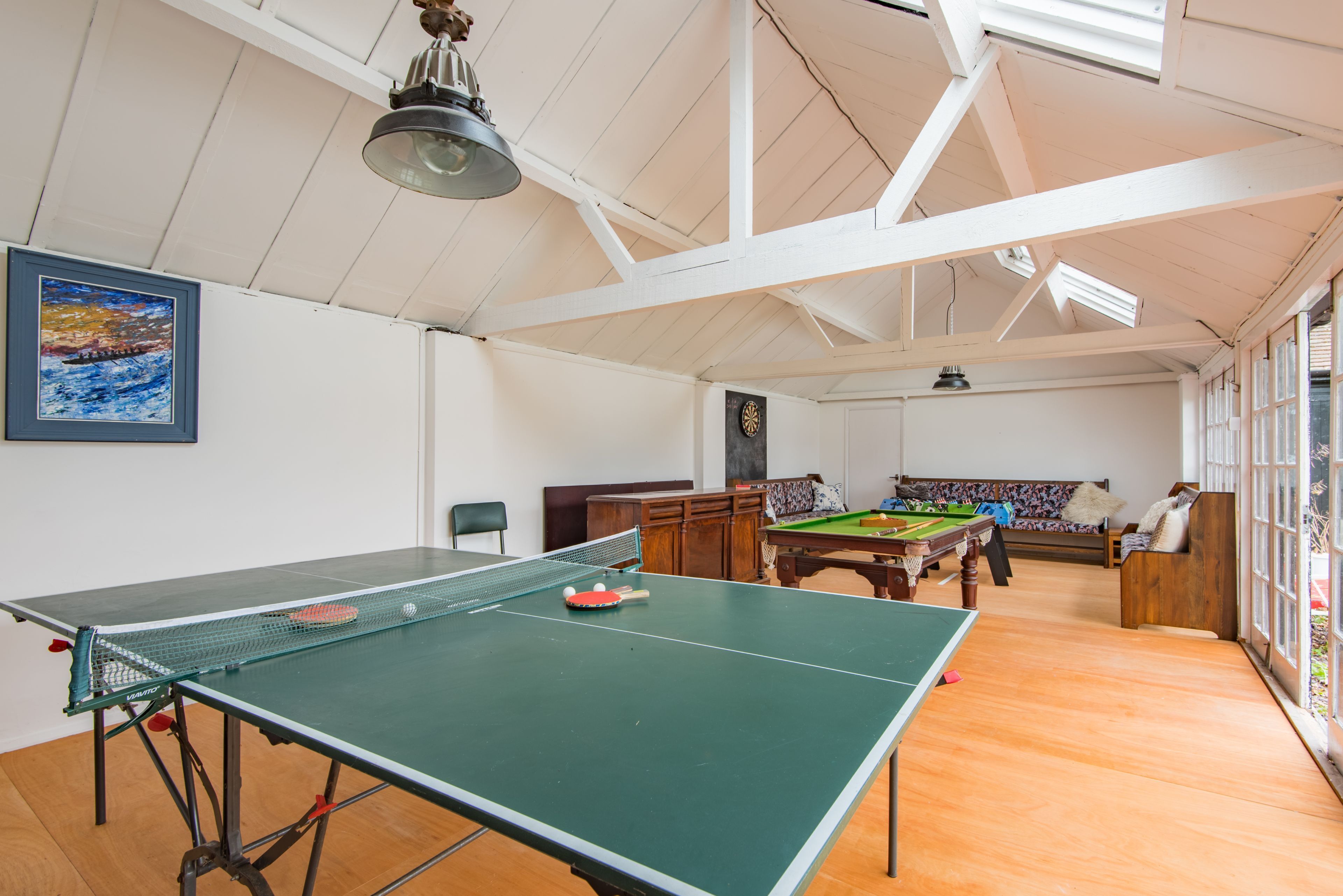 A room with a ping pong table, billiards table, and a billiard cue rack.