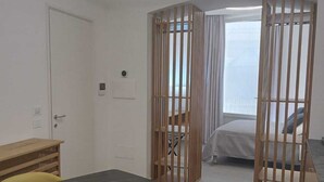 A modern room with a dining table, yellow chairs, a bed with a view, and a partition with vertical slats. - De Guidani Experience (Lecce)