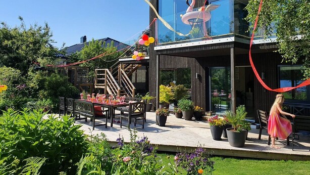 Une maison moderne dotée d’un balcon en verre, d’un espace salon extérieur et de plantes en pot.