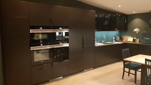 Une cuisine moderne avec des meubles de couleur sombre, des appareils en acier inoxydable et un coin repas comprenant une table et des chaises en bois.