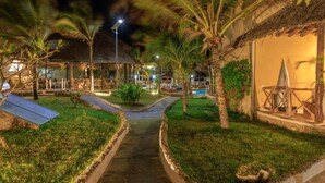 Un quartier de villégiature animé la nuit, avec un sentier pavé, des palmiers et des constructions à toits de chaume.