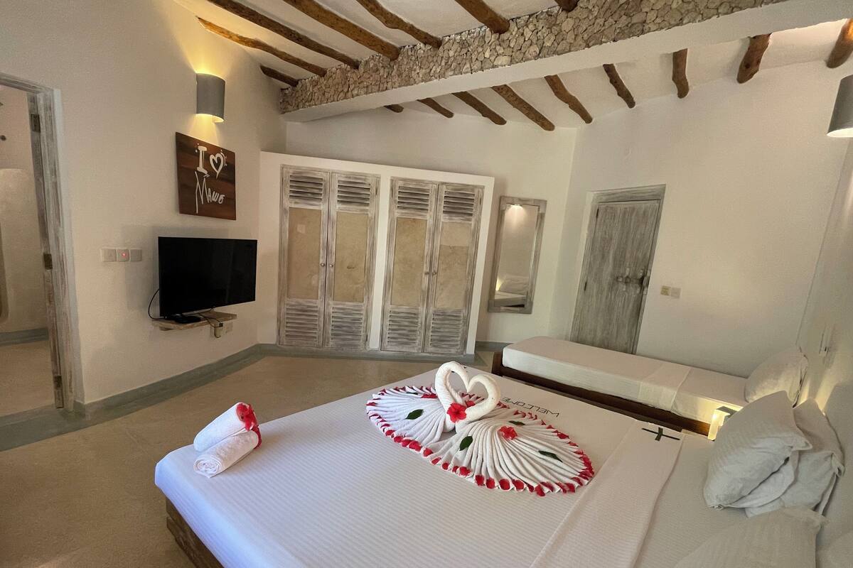 Quarto com cama, televisão, parede de pedra e teto de madeira.