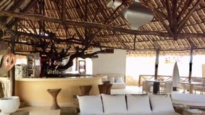 Un espace extérieur aménagé avec un toit de chaume, comprenant un canapé, des tables et un bar.