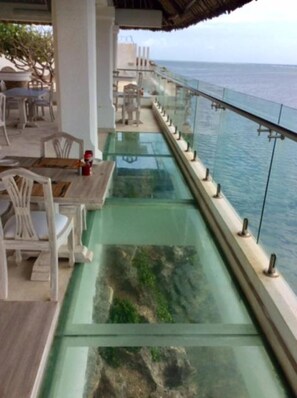 A glass-bottomed walkway with a view of the ocean, wooden furniture, and a railing. - Mawe Zuri Resort  (Watamu)