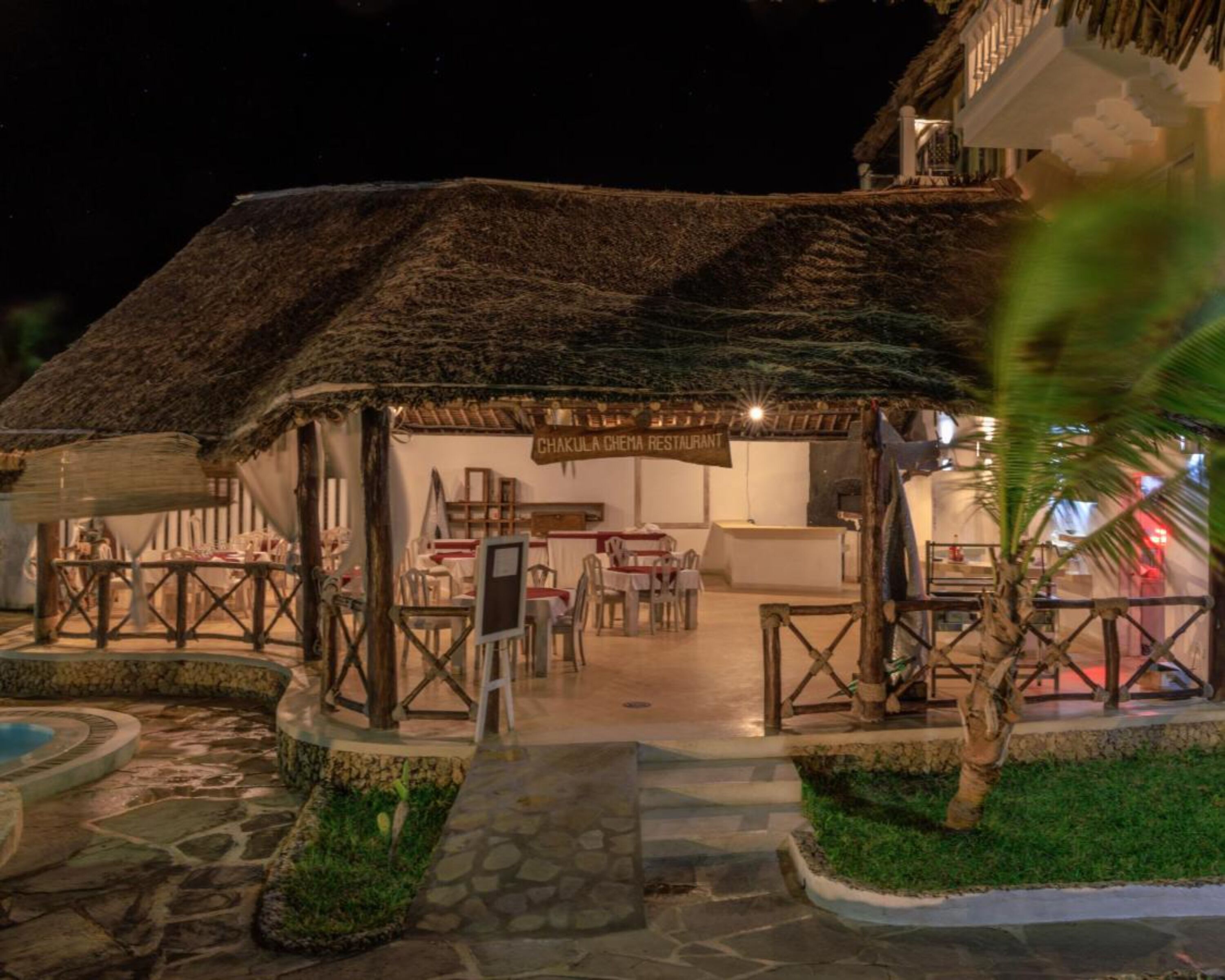 Un ristorante con tetto di paglia, posti a sedere all'aperto e un vialetto in pietra che conduce all'ingresso.