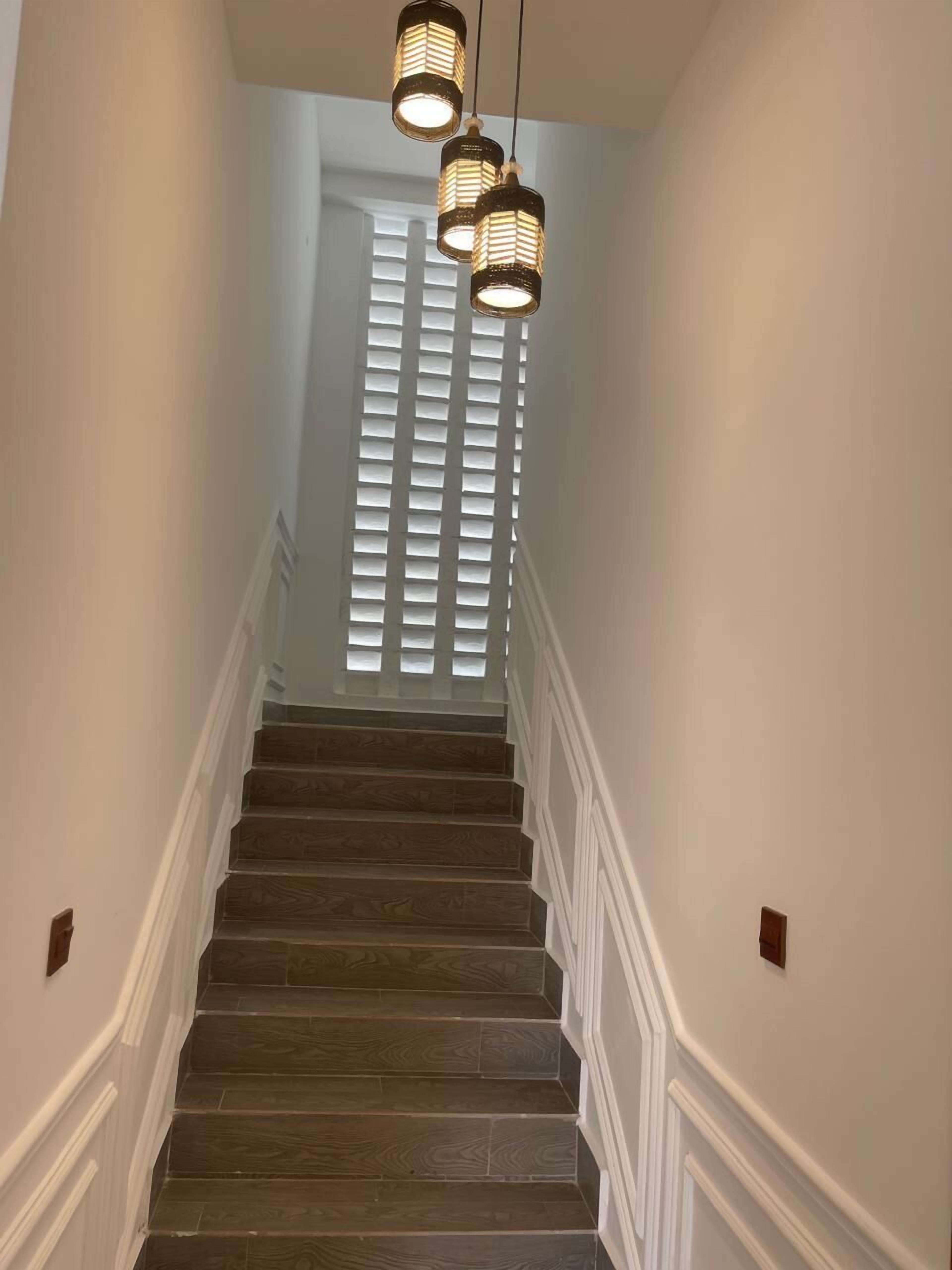 Eine Treppe mit Holzboden und weißen Geländern, die zu einem Raum mit einem Fenster und Jalousien führt.