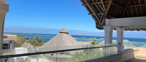 A balcony with a view of the ocean and a thatched-roof structure.