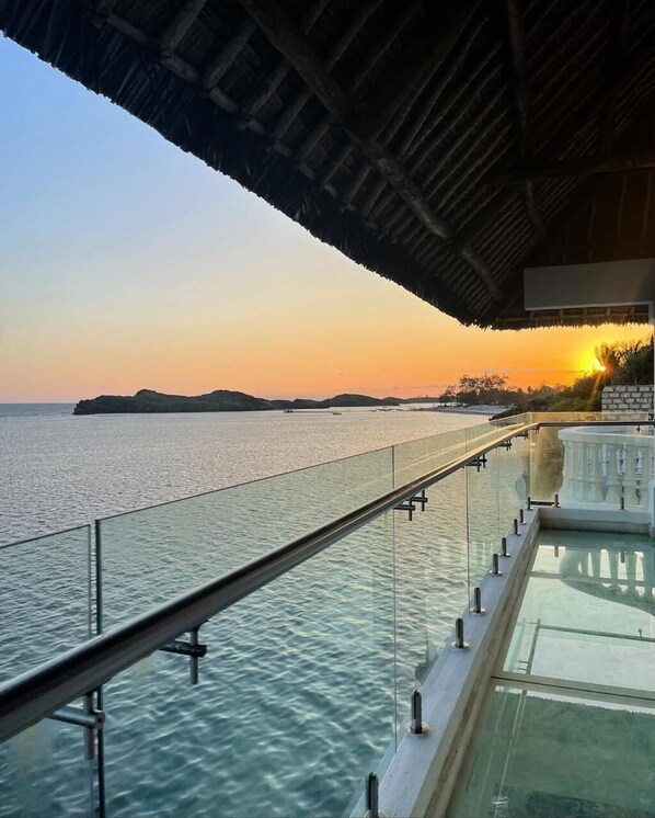 A glass balustrade overlooking a body of water with a sunset in the background. - Mawe Zuri Resort (Watamu)