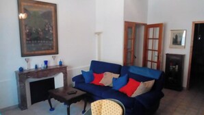 Un salon avec un canapé bleu, une petite table, une cheminée et une porte donnant sur une autre pièce.