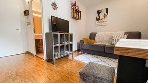 Una sala de estar con un sofá gris, un televisor sobre un mueble, una mesita y un adorno en la pared.