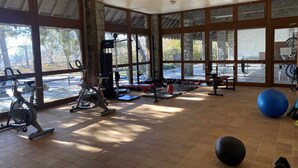 Un gimnasio espacioso con amplias ventanas, equipamiento de ejercicio y vistas al exterior.