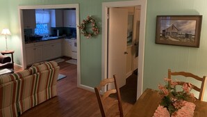 A living room with a striped sofa, a wooden dining table with a vase of flowers, a kitchen in the background, and a door with a wreath. - Queen Anne's Revenge At The Beach 3 Bedroom Cottage by RedAwning (Kitty Hawk)