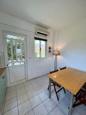 A room with a wooden table and chairs, a white door with glass panels, and a window with a view of greenery.