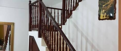 Una escalera con balaustres de madera y una pared blanca con un reloj decorativo y un cuadro enmarcado.