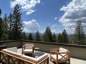 A rooftop terrace with outdoor furniture, a view of trees and mountains, and a clear sky.