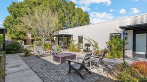 Un espace patio extérieur moderne, doté de sièges et d’un barbecue, entouré de verdure et d’un bâtiment en métal.