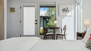 Une chambre d’hôtel avec un lit, une table et des chaises, un balcon agrémenté de plantes et des œuvres d’art aux murs.