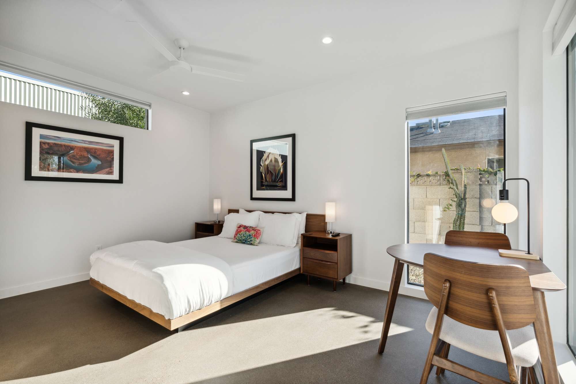 Quarto moderno com cama, mesas de cabeceira, uma cadeira e vista para o exterior.