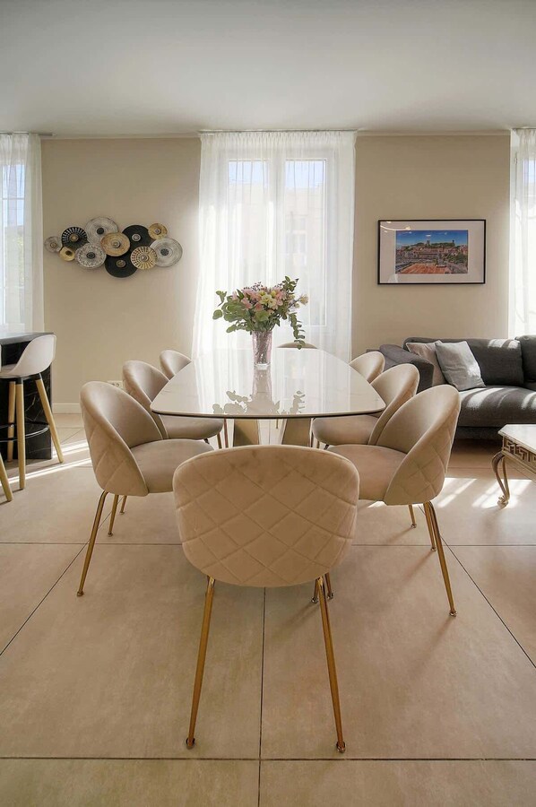 A modern dining area with a round glass table surrounded by six chairs with gold legs.