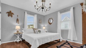 Un dormitorio con una cama, dos mesitas de noche con lámparas, un candelabro y una ventana con cortinas.