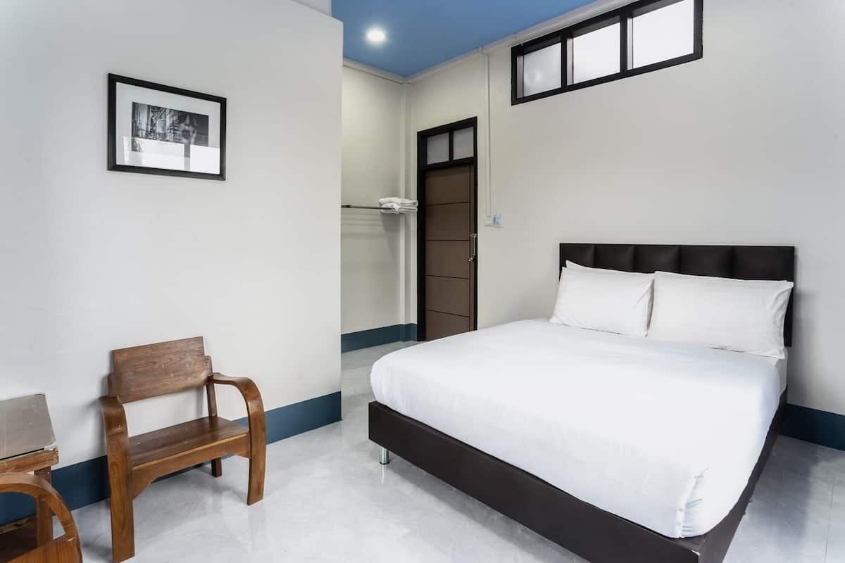 A bedroom with a bed, a wooden chair, a framed picture on the wall, and a door leading to a bathroom.
