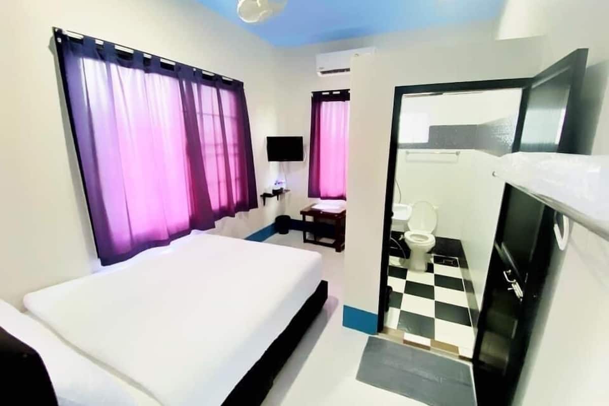 A hotel room with a bed, a desk, a chair, a television, and a bathroom with a checkered floor.