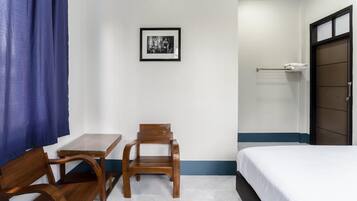 A hotel room with a bed, a small table, two wooden chairs, a framed picture on the wall, and a towel rack.