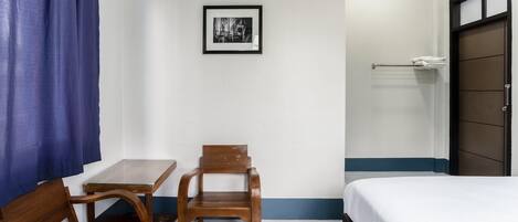 A hotel room with a bed, a small table, two wooden chairs, a framed picture on the wall, and a towel rack.