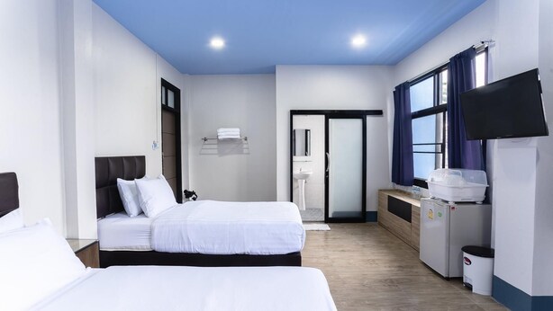 A hotel room with two beds, a TV, a mini-fridge, a sink, and a window with curtains. - Udomsuk Hotel (Satun)