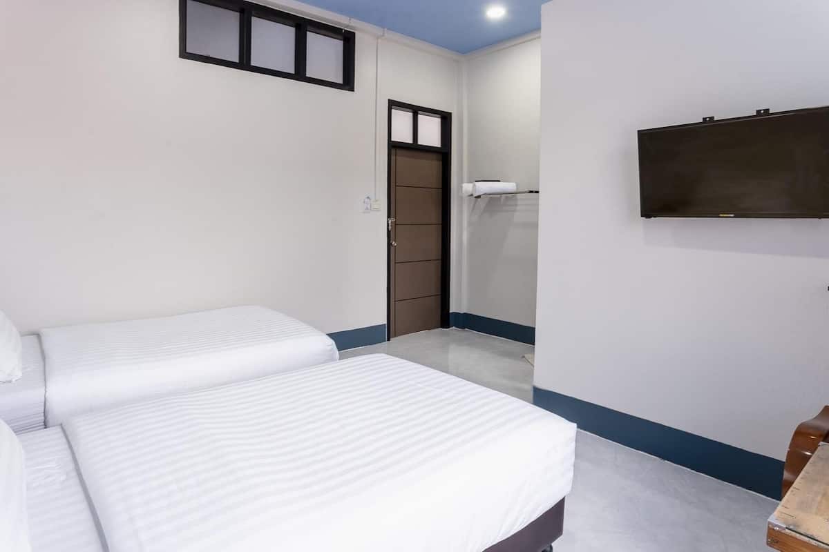 A hotel room with two beds, a wardrobe, a TV mounted on the wall, and a small wooden table.